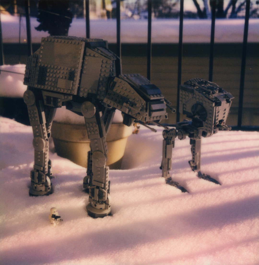 Lego Star Wars versions of an AT-AT and an AT-ST depicted in the snow on a city balcony.